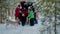 Happy family looking New Year gift in car trunk in winter forest. Mom, dad, son and daughter in red Christmas hat having