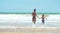 Happy family mom and baby running barefoot on wet sand, rear view. Mom and baby holding hands together runing on beach.