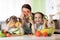 Happy family mother and kids having fun with food vegetables at kitchen holds pepper before their eyes like in glasses