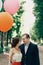 Happy family portrait, newlywed couple hugging in a sunny park in the summer, handsome groom looking at happy bride with balloons