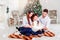 Happy family reading Christmas fairy tales near the Xmas tree. Living room decorated by Christmas tree and present gift box