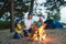 Happy family roasting sausages over campfire. camping and tourism concept