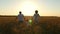 Happy family running through a wheat field in the sun at sunset