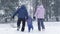A happy family runs holding hands towards the forest during a snowfall in winter. Leisure, tourism and games in nature