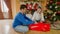 Happy family sitting on floor and wrapping Christmas presents in paper and decorating with ribbons