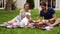 Happy family sitting on a plaid at the picnic on the green beautiful meadow on a sunny day. Their son is sitting near