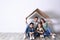 Happy family sitting under cardboard roof near wall, space for text. Insurance concept