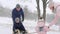 Happy family sledding on snowy winter day. Daughter helps father and mother to pull sled with son on snowfall. Boy