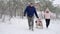 Happy family sledding on snowy winter day. Father and mother pull sled with son and daughter on snowfall. Boy and girl