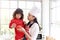 Happy family, smiling beautiful Asian mother wears cute red heart apron and chef hat holds daughter while little girl holds apple