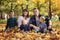 Happy family with three children are sitting in the autumn park among the fallen yellow foliage. Love and tenderness. Camping.