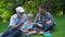 Happy family of three generation - father, grandfather and blond son sitting on grass at park with books learn to read