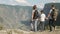 Happy family of tourists come to the peak of the mountain and rejoice raising their hands up.