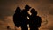 Happy family tourists silhouette at sunset hug kissing. Teamwork travel concept. Man and woman couple with backpacks