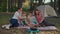 Happy family of two moms and two sons cooking pop corn on frying pan sitting on picnic blanket with Siberian Husky dog