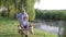 Happy family vacation in countryside, father fools around with his son in wheelbarrow near river with reeds