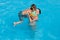 Happy family vacation of young woman mother lifting her little kid in armbands and goggles in outdoor fresh water blue pool in