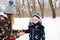 Happy family during walk at snowy forest. Mother helps her little son put on a warm gloves. Happy winter holidays. Snowy winter