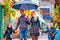 Happy family walking under the rain on colorful street