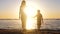 A happy family walks along the seashore against the backdrop of a beautiful sunset. A mother holds her son`s hand and