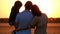 Happy family watching the sunset, standing in a wheat field. A man holding a child in his arms. A woman hugs a man