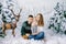 Happy family of young parents and a baby in winter sweaters in a fake winter forest, in the photo zone in the Studio. They are smi