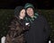 Happy father and daughter standing in the cold in front of bushes with Christmas lights