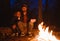 Happy father and his son warm themselves by the fire sitting in an embrace on logs in a hike in the forest at the night.