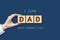Happy father`s day background. Female hand with the word, dad written on wooden blocks. Dark background Congratulatory background