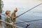 Happy father and son together fishing from wooden stairs, look concentrated, enjoying to spend time together, wants to catch lots