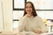 Happy female employee sits at table in office smiling