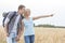 Happy female hiker showing something to man on field against clear sky