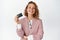 Happy female manager shows credit card and smiles pleased, stands in suit against white background