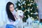 Happy female person sitting with white labrador near decorated Christmas tree.