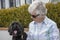 Happy female senior woman sitting with black cockapoo puppy outdoors