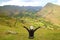 Happy female traveler raising arms on the mountain slope of Pisac archaeological park, Sacred Valley of the Incas, Peru