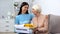 Happy female volunteer and aged woman holding donation box, humanitarian aid