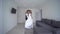 Happy fiance carries bride on hands in white dress and rotate at new apartment on wedding day