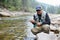 Happy fisherman holding trout while sitting near river