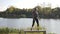 Happy fitness model girl dancing and spreading positive energy up on a bench in the park in nature near a lake in sunlight