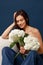 A happy fragile girl in blue jeans and a beige corset sits on a chair and holds a bouquet of hydrangeas in her hands. Blue