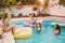 Happy friends having fun in swimming pool during summer vacation - Young people relaxing and floating on air lilo