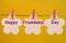 Happy Friendship Day message greeting across white flower tags hanging from pegs on a line