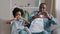 Happy funny african american family mature father and little daughter sitting on sofa in room smiling make heart shape