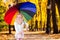 Happy funny beautiful blonde with blue eyes child with rainbow colorful umbrella in the autumn park. Girl kid playing on