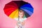 Happy funny beautiful blonde with blue eyes child with rainbow colorful umbrella in pink background in studio. Girl kid