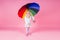 Happy funny beautiful blonde with blue eyes child with rainbow colorful umbrella in pink background in studio. Girl kid