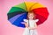 Happy funny beautiful blonde with blue eyes child with rainbow colorful umbrella in pink background in studio. Girl kid