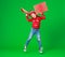 Happy funny child girl in red Christmas hat   with gift jumping on green   background
