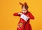 Happy funny child girl in red Christmas reindeer costume with gift surprise sock on yellow   background